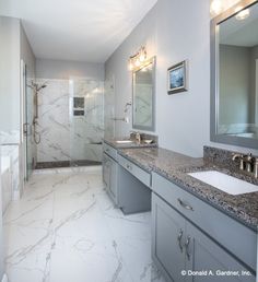 a large bathroom with marble counter tops and gray cabinets, along with a walk in shower