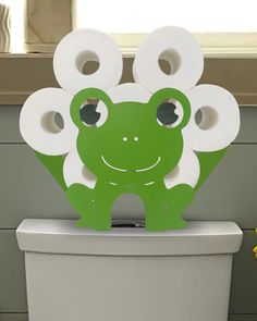 a green frog sitting on top of a toilet next to two rolls of toilet paper