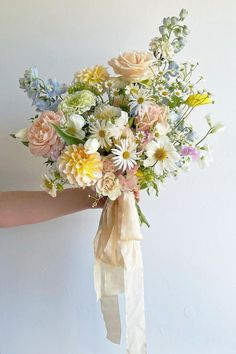 a woman holding a bouquet of flowers in her hand with a white ribbon around it