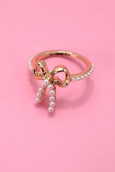 Introducing our Gold Pearl Bow Ribbon Ring, a delightful fusion of elegance and charm. This exquisite ring features a lustrous pearl nestled within a gracefully crafted bow and ribbon design, adding a touch of sophistication to your jewelry collection. Elevate your style with the delicate beauty of the Gold Pearl Bow Ribbon Ring, a symbol of refined taste and grace. DIMENSION:size: 7Metal finish: Gold Platingproduct: Lead & Nickle Compliantanti-tarnish: Double E-coating Girly Rings, Coquette Diy, Ribbon Ring, Ring My Bell, Antique Candles, Pearl Engagement Ring, Pearl Bow, Kawaii Jewelry, Bow Ring