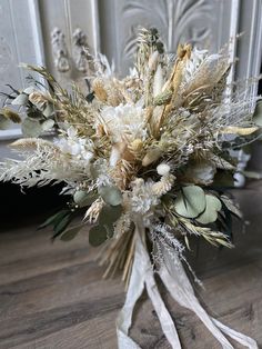 a bridal bouquet with white flowers and greenery on a wooden floor in front of a door