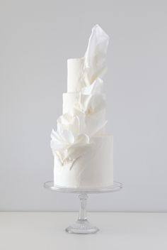 a three tiered white wedding cake with ruffles