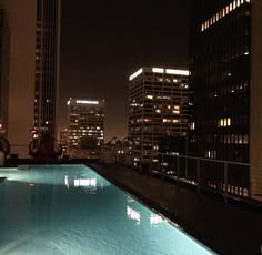 an empty swimming pool in the middle of a city at night with skyscrapers lit up