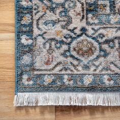 a blue and white rug with fringes on top of a wooden floor next to a wall