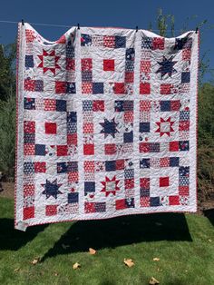 a red, white and blue quilt hanging from a clothes line in the grass on a sunny day