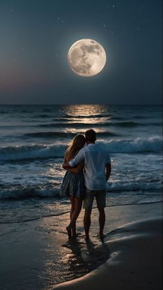 a man and woman standing on the beach at night with the moon in the background