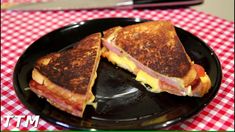 a grilled cheese and bacon sandwich on a black plate with a red checkered tablecloth