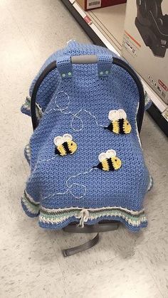 a blue crocheted baby seat cover with two bees on it in a store