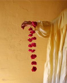 a person holding flowers in front of a yellow wall with red petals hanging from it