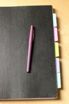 a pink pen sitting on top of a notebook next to four colored sticky notes in it