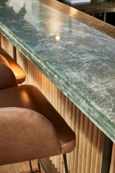 a bar with two brown leather chairs and a green marble counter top in the background