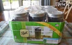 four jars with lids are sitting on a table in front of a box that says ball