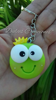 a hand holding a green keychain with a smiley face and crown on it