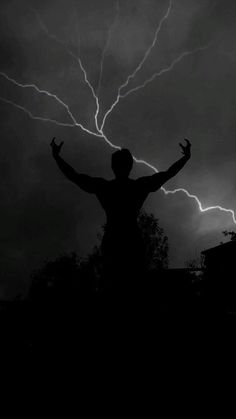 a man is standing in the dark with his arms wide open while lightning strikes behind him