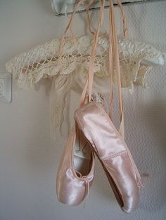 two ballet shoes hanging on a wall next to a lace hanger with three pairs of pink ballet shoes