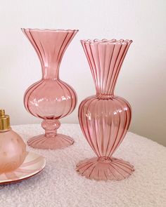 three pink glass vases sitting on top of a table next to a candle holder