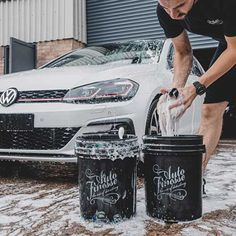 a man washing his car in the snow with two buckets next to it,