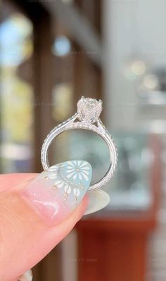 a woman's hand holding an engagement ring with a flower design on the side