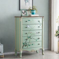 a green chest of drawers with flowers and birds painted on the front, sitting in a living room