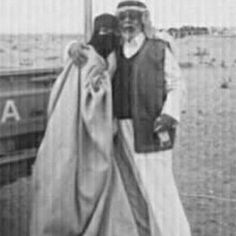 an old black and white photo of two people standing next to each other in front of the ocean