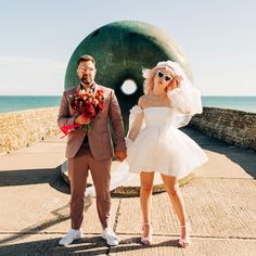 a man and woman dressed in wedding attire standing next to each other near the ocean