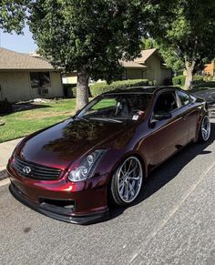 a maroon car parked on the side of a road next to a tree and house