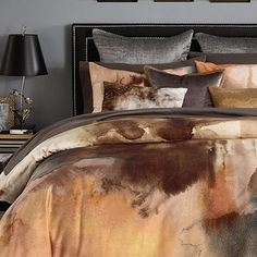 a bed covered in lots of pillows next to a night stand with pictures on the wall