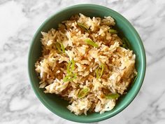 a green bowl filled with rice on top of a white countertop next to a marble table