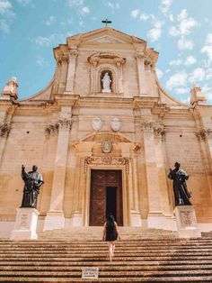 a woman standing in front of a church with statues on the steps next to it