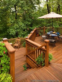 a wooden deck with chairs and an umbrella in the middle surrounded by greenery on both sides