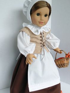 a doll is holding a basket and wearing a white dress with brown trimmings