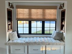 a window seat with pillows on it in front of a window and bookshelves