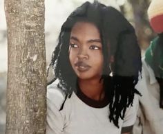 a woman with dreadlocks standing next to a tree