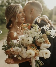 a bride and groom kissing in front of the camera with flowers on their bouquets