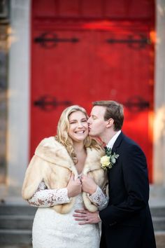 a bride and groom standing in front of a red door with fur stolers on their shoulders