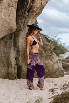 a woman standing on top of a sandy beach next to a large rock formation and wearing a black hat