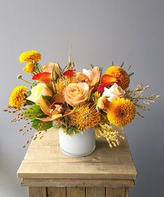 a white vase filled with orange and yellow flowers on top of a wooden table next to a gray wall