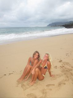 two women in bikinis sitting on the beach