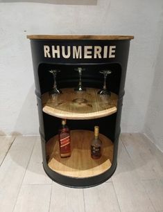 a barrel with three bottles on it and some wine glasses in the bottom shelf that says rhumerie