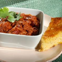 a white bowl filled with chili next to a piece of bread