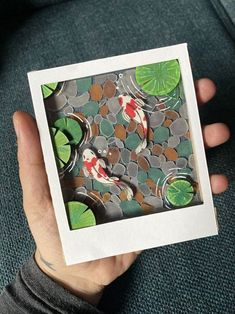 a person holding up a small card with fish and lily pads on the inside of it