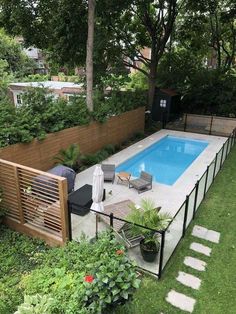 an above ground swimming pool surrounded by greenery and wooden fence, with chairs around it