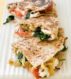 two quesadillas on a white plate with tomatoes and spinach, one cut in half