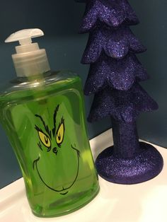 a green liquid bottle with a grin face on it next to a purple christmas tree