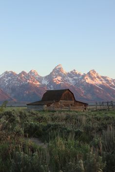 a barn sits in the middle of an open field with mountains in the background at sunset