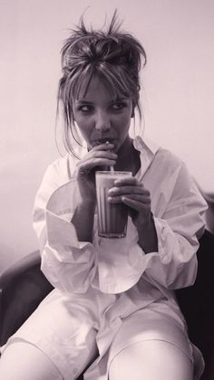 a woman sitting in a chair drinking from a cup with her hand on her mouth