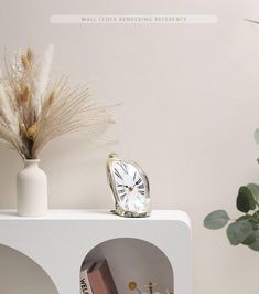 a white clock sitting on top of a shelf next to a vase filled with flowers