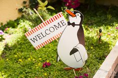 a penguin holding a welcome sign in the grass