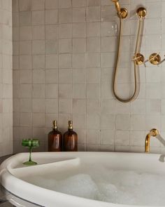 a bathtub filled with water next to a shower head and two soap dispensers