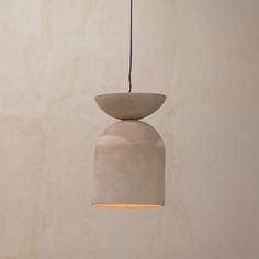 a light that is hanging from the ceiling in front of a wall with a vase on it